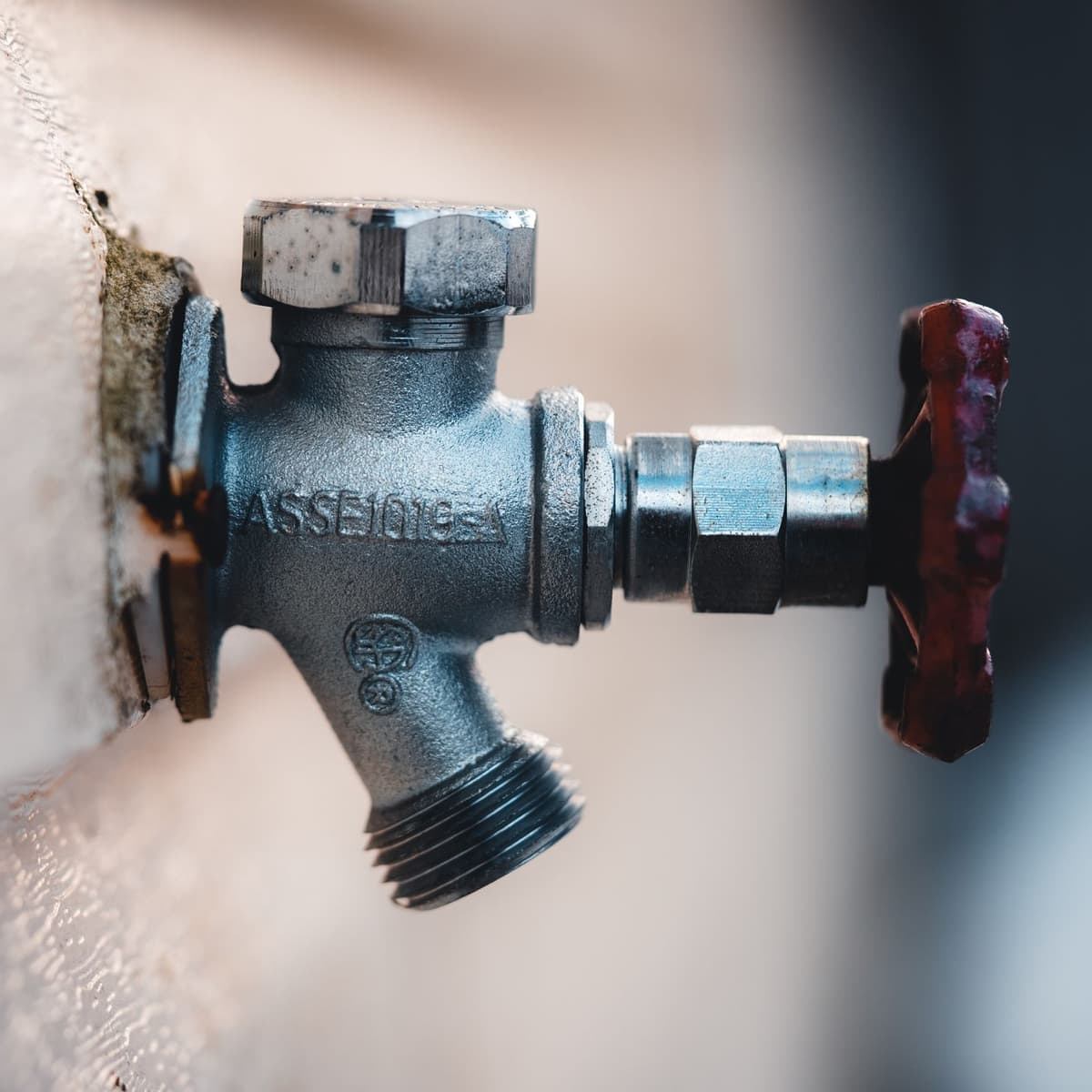 Hand closing the main water shutoff on the side of a stucco house